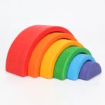 Un ensemble de blocs empilables arc-en-ciel en bois colorés disposés par ordre de taille sur un fond blanc.
