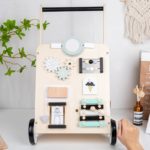 Un Trotteur pousseur bébé - multi-activités - Couleurs pastel s'amuse avec un chariot multi-activités en bois.