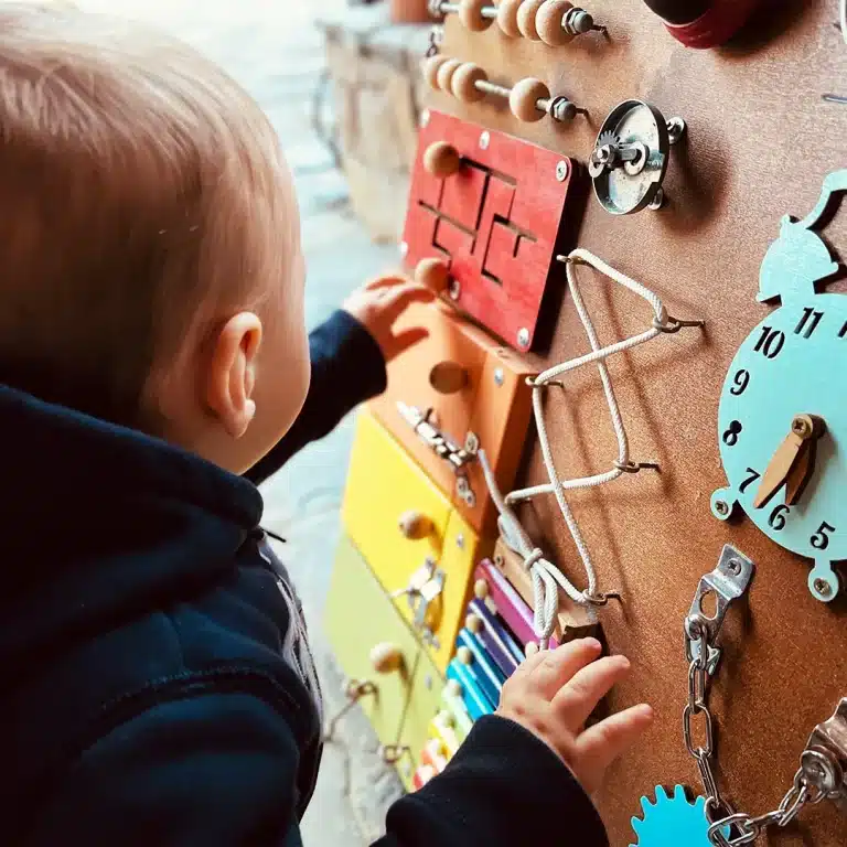 Un enfant joue avec une planche de bois pleine de jouets.