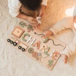 Deux enfants sont assis sur un tapis léger, jouant avec un Puzzle Personnalisé Prénom en Bois qui épelle « CHARLIE » et présente des formes amusantes comme un train, un cactus et un palmier.