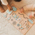 Deux enfants jouent sur un tapis beige avec le Puzzle Personnalisé Prénom en Bois, personnalisé avec "Charlie" et des pièces amusantes sur le thème nautique.