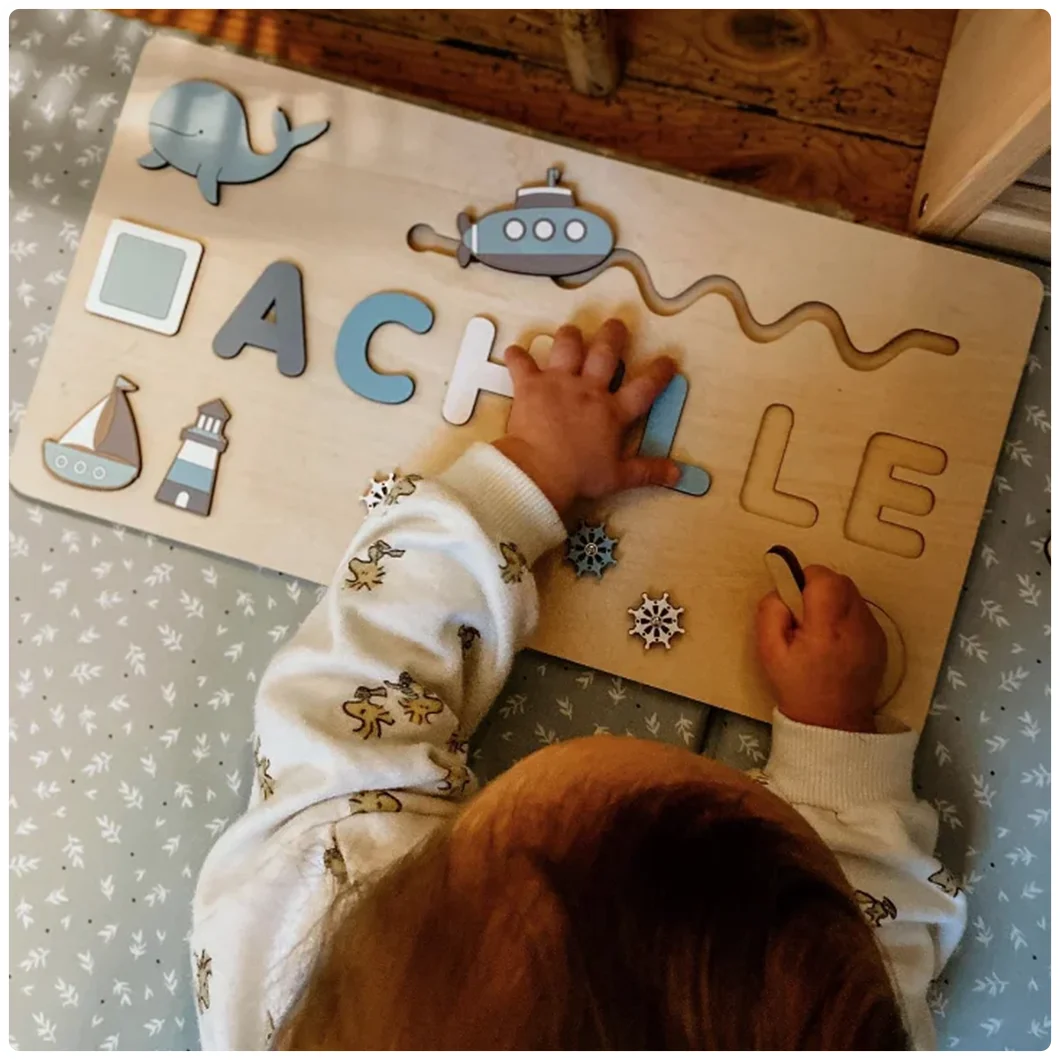 Un enfant joue avec un puzzle en bois personnalisé portant le nom "ACHILLE" et des formes telles qu'une baleine, un sous-marin, un bateau et un phare.