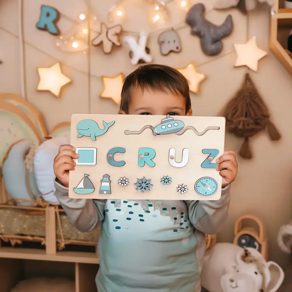Un jeune enfant tient un puzzle en bois sur lequel est écrit « CRUZ » avec des pièces sur le thème de l'océan dans une salle de jeux confortable et bien décorée.