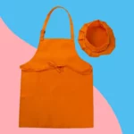 Les Tablier et Toque de Cuisine pour Enfant en orange vif sont présentés sur un fond bleu et rose éclatant.