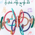 Mains tenant un Hochet multi fonction- Montessori, un jouet sensoriel multicolore composé de boucles et de perles, sur fond de notes de musique et d'ondes sonores.