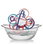 Le Hochet multi fonction- Montessori est un jouet vibrant qui flotte dans un bol en verre transparent rempli d'eau.