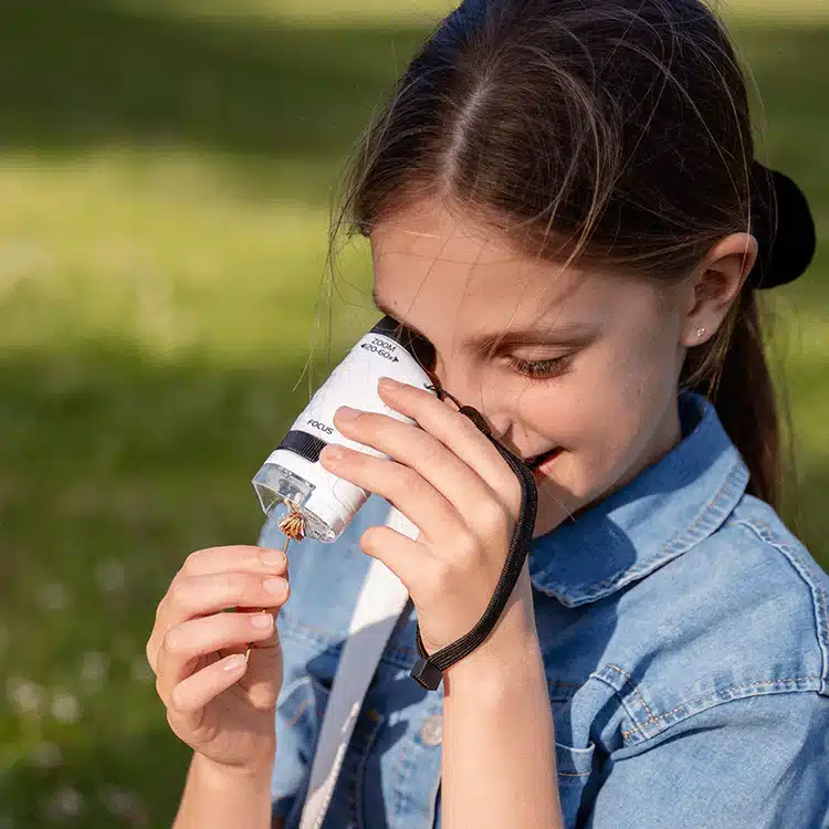 Une fille en chemise en jean examine un petit objet à travers un microscope portable à l'extérieur.