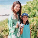 Une femme et son enfant se promènent sur un sentier de plage, appareils portables à la main, au cœur d'une végétation luxuriante. Au loin, l'océan nous attire par sa beauté sereine.