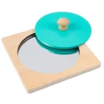 Une base carrée en bois avec un miroir circulaire encastré, semblable au miroir en bois Puzzle Montessori, est ornée d'un couvercle rond vert surmonté d'une élégante poignée en bois.