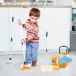 Un enfant tient joyeusement un ensemble de balai et pelle à poussière Set de Ménage pour Enfants - Imitation Nettoyage - 12 pièces, avec des produits de nettoyage éparpillés tout autour, debout à l'intérieur.