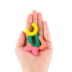 Une main tient quatre lettres en mousse vibrantes : un C jaune, un U vert, un X rouge et un T rose. Ces lettres colorées évoquent les outils Planche Montessori – Math et anglais, apparaissant sur un fond blanc pour engager les jeunes apprenants dans des activités d'anglais amusantes.