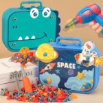 Boîte à outils Montessori pour enfants sur le thème de l'espace, comprenant des boulons en plastique colorés, une visseuse à piles et un tournevis posés sur une table. Les boîtiers bleus et verts présentent des motifs ludiques de fusées et de dinosaures.