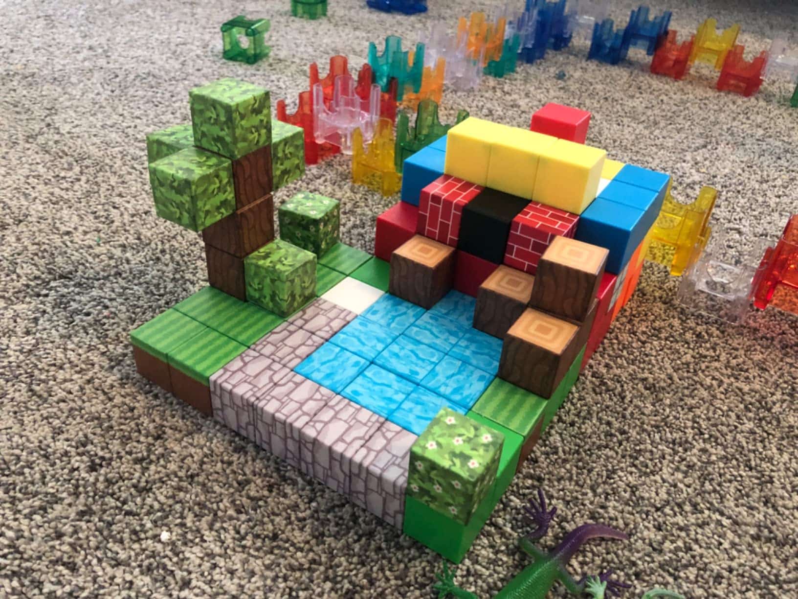 Une structure composée de blocs de jouets colorés, comprenant un arbre, des blocs bleus ressemblant à de l'eau et d'autres blocs disposés sur un sol recouvert de moquette.