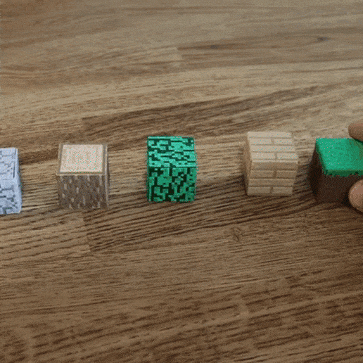Une main pousse une série de blocs sur le thème de Minecraft disposés en ligne, provoquant un effet domino sur une surface en bois.