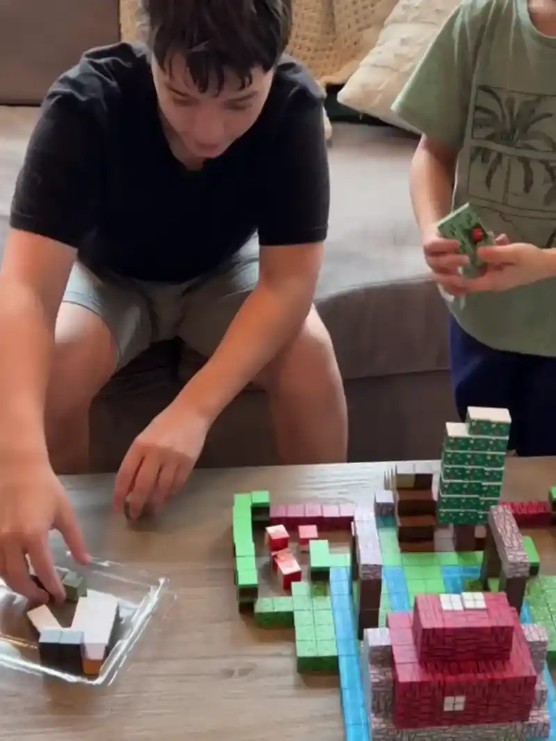 Deux enfants sont assis à une table et construisent une structure en blocs avec des blocs rectangulaires de différentes couleurs et motifs.